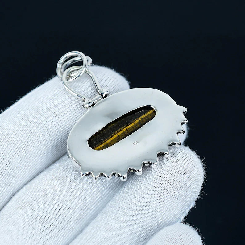 Silver pendant with a central stone held in a white glove against a black background