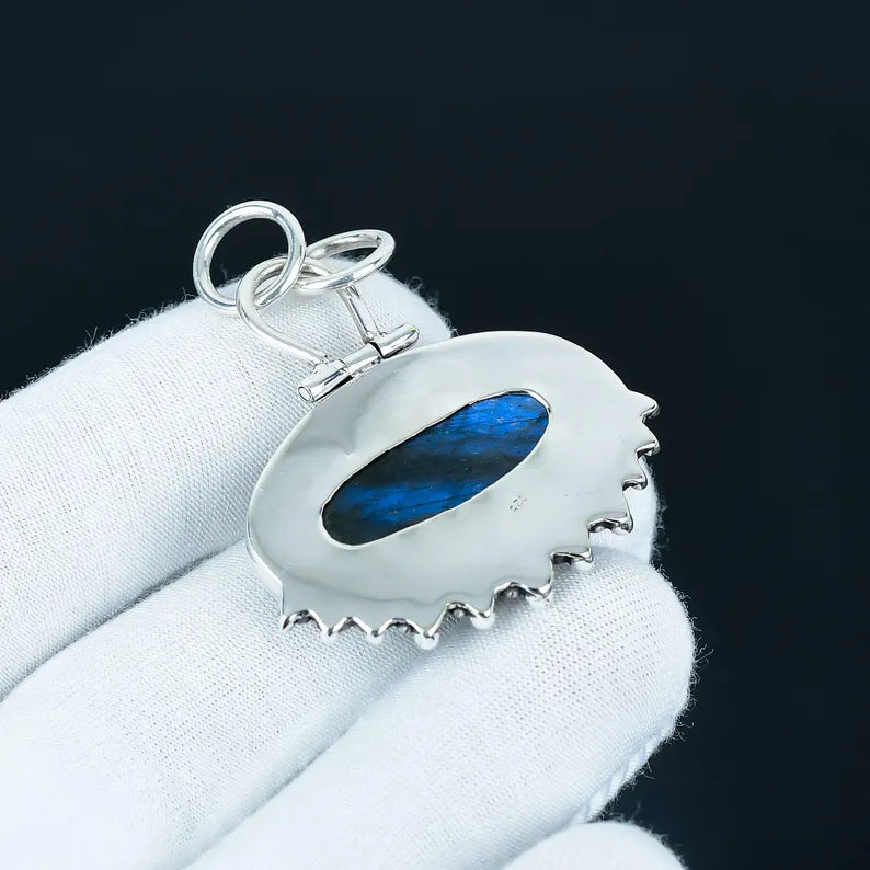 Silver pendant with a blue stone on a white stand against a black background
