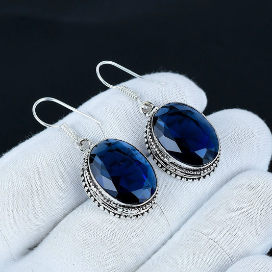 Blue gemstone earrings on a white glove with a dark background