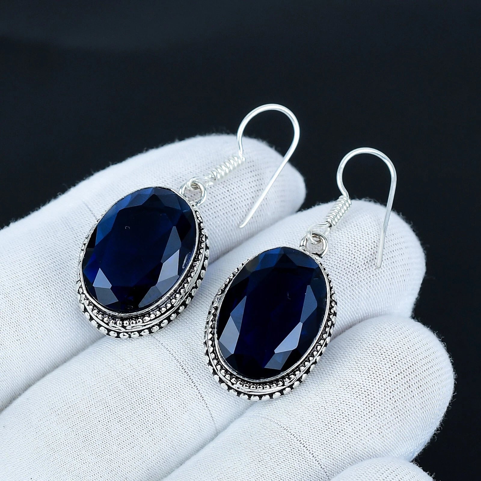 Pair of blue gemstone earrings on a white glove with a dark background