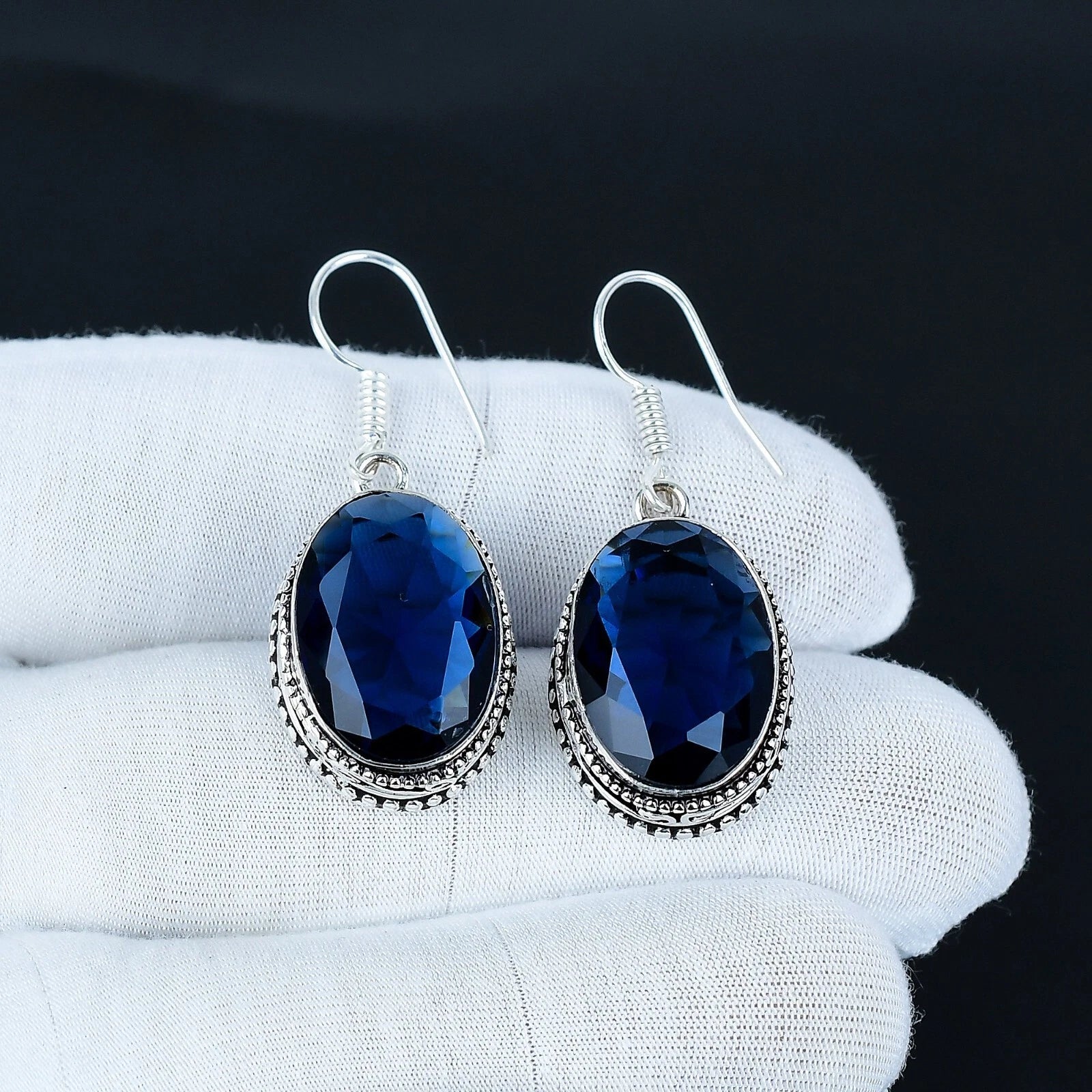 Blue gemstone earrings on a white glove with a black background