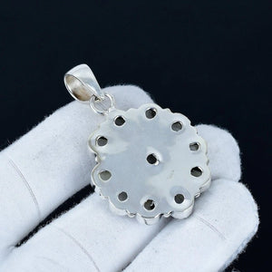 Silver pendant held in a white glove against a black background