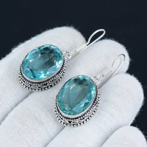 Pair of silver earrings with blue gemstones held on a white cloth background