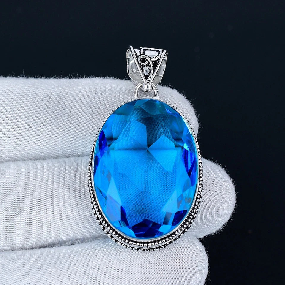 Blue gemstone pendant on a white cushion with a black background