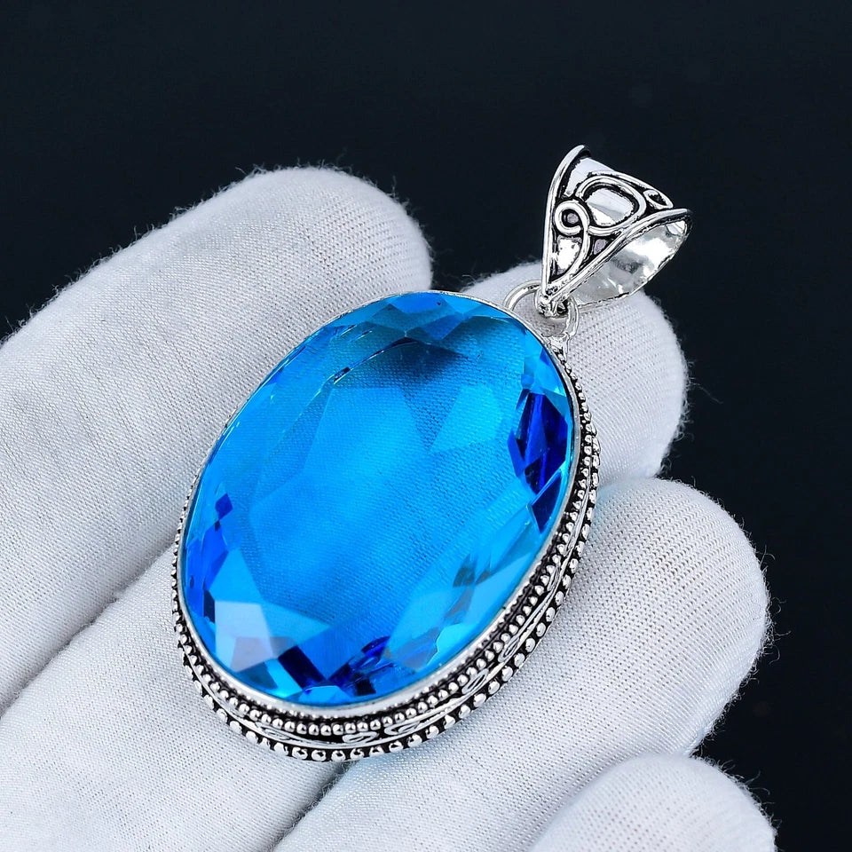 Blue gemstone pendant held by a gloved hand against a black background