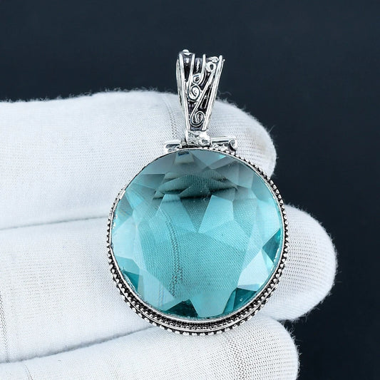 Aqua Apatite pendant with silver frame held by a gloved hand against a dark background